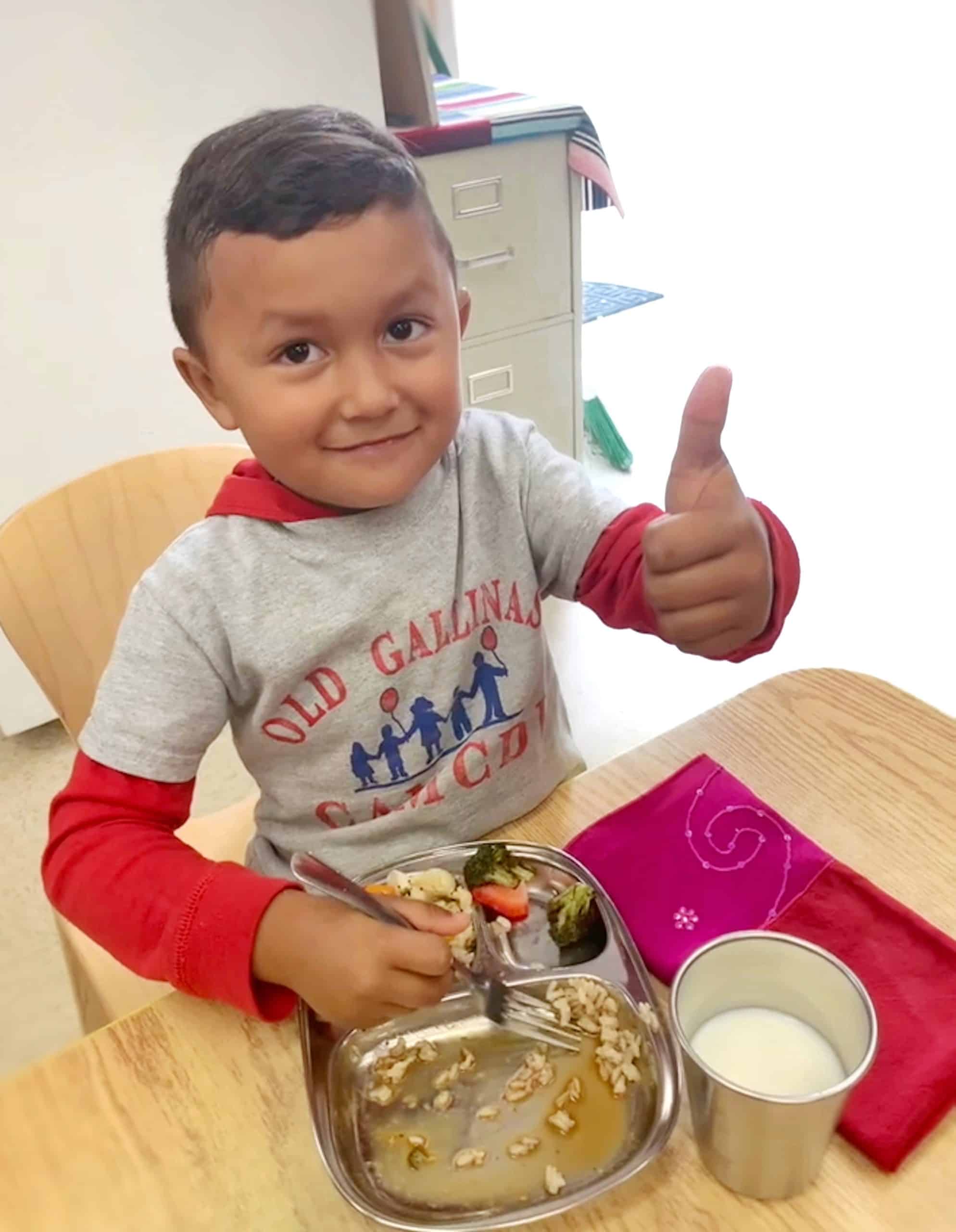 A student gives a thumbs up while eating an organic lunch with organic milk provided by Conscious Kitchen.