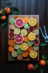 An assortment of citrus fruit slices laid oout on a wooden cutting board. The fruits are oranges, limes, lemons, blood oranges, and grapefruit.