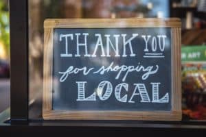A chalkboard sign hanging in a window that reads "Thank you for shopping local" in handwritten calligraphy.