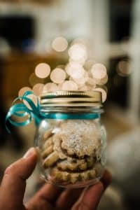 A glass mason jar filled with small cookies, with a blue ribbon tied around it.