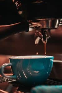 A close up image of espresso dripping into a teal coffee cup.