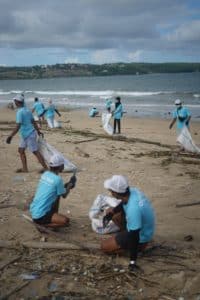 A group of people in light blue tee shirts pick up trash on the beach.