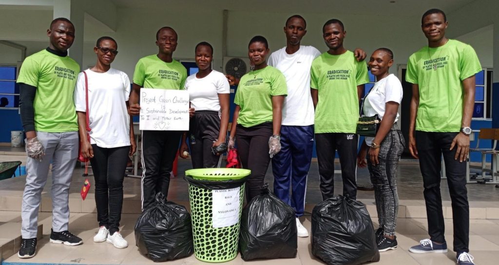 Promise and his sustainability team standing around litter they picked up. Promise holds a sign reading Project Green Challenge.